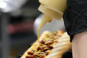 Preparing an easy hot dog sandwich by adding sauce to the bun with sausage and toppings